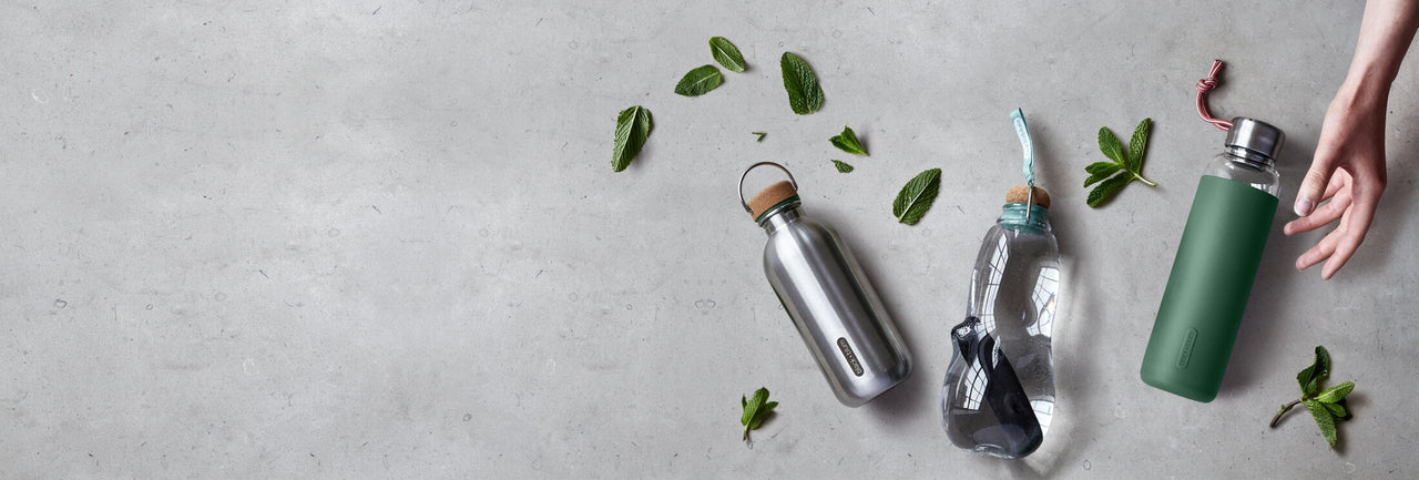 Reusable leak proof water bottles on grey bench with mint leaves